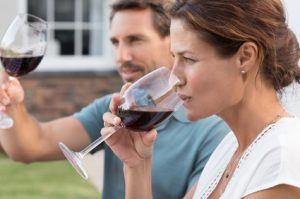 Portrait of young woman drinking red wine while man raising a toast. Mature couple enjoying drinks in the park. Couple enjoying picnic with wine.